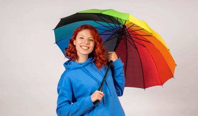 Młoda kobieta o rudych włosach, uśmiechnięta, trzymająca kolorowy parasol.