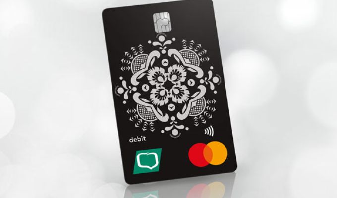 Czarna karta płatnicza MasterCard PayPass z białym folkowym wzorem oraz z logo Grupy BPS, ustawiona w pionie pod kątem na jasnym, rozmytym tle.
