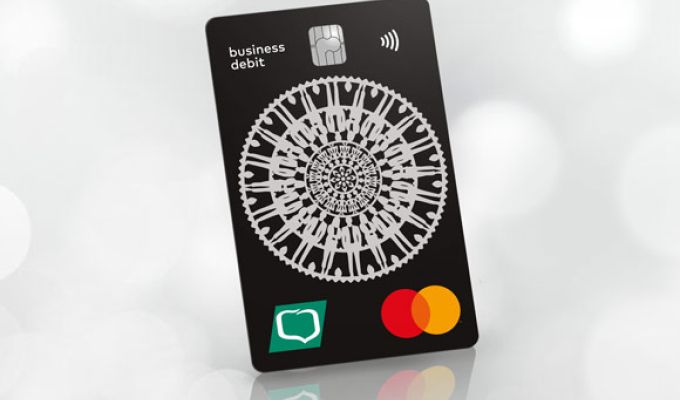 Czarna karta płatnicza MasterCard Business PayPass z białym folkowym wzorem oraz z logo Grupy BPS, ustawiona w pionie pod kątem na jasnym, rozmytym tle.